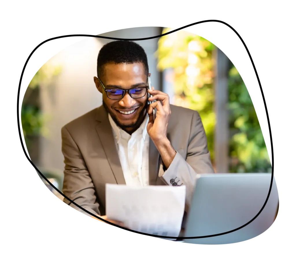 Smiling professional on a phone call reviewing documents at a laptop, embodying successful sales and recruiting.